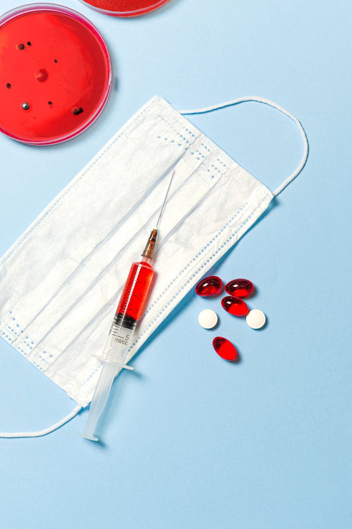 Face mask, syringe, and pills on a blue background, symbolizing healthcare and medical research.