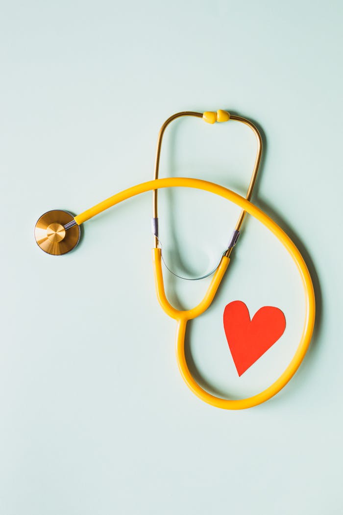 services-02 Yellow stethoscope arranged with a red heart cutout on a light green background, symbolizing heart health.